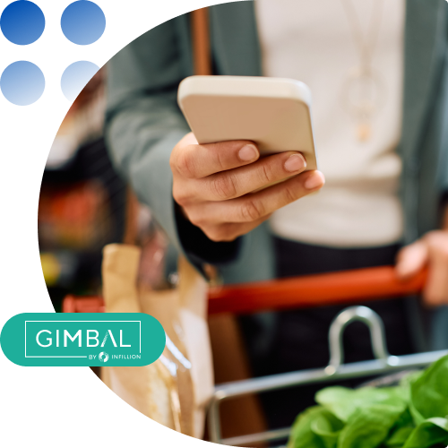 Person using a smartphone while pushing a grocery cart in a supermarket, with fresh produce visible.