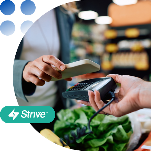 Customer paying with a card at checkout; cashier taps a card reader near vegetables with the Strive logo visible.