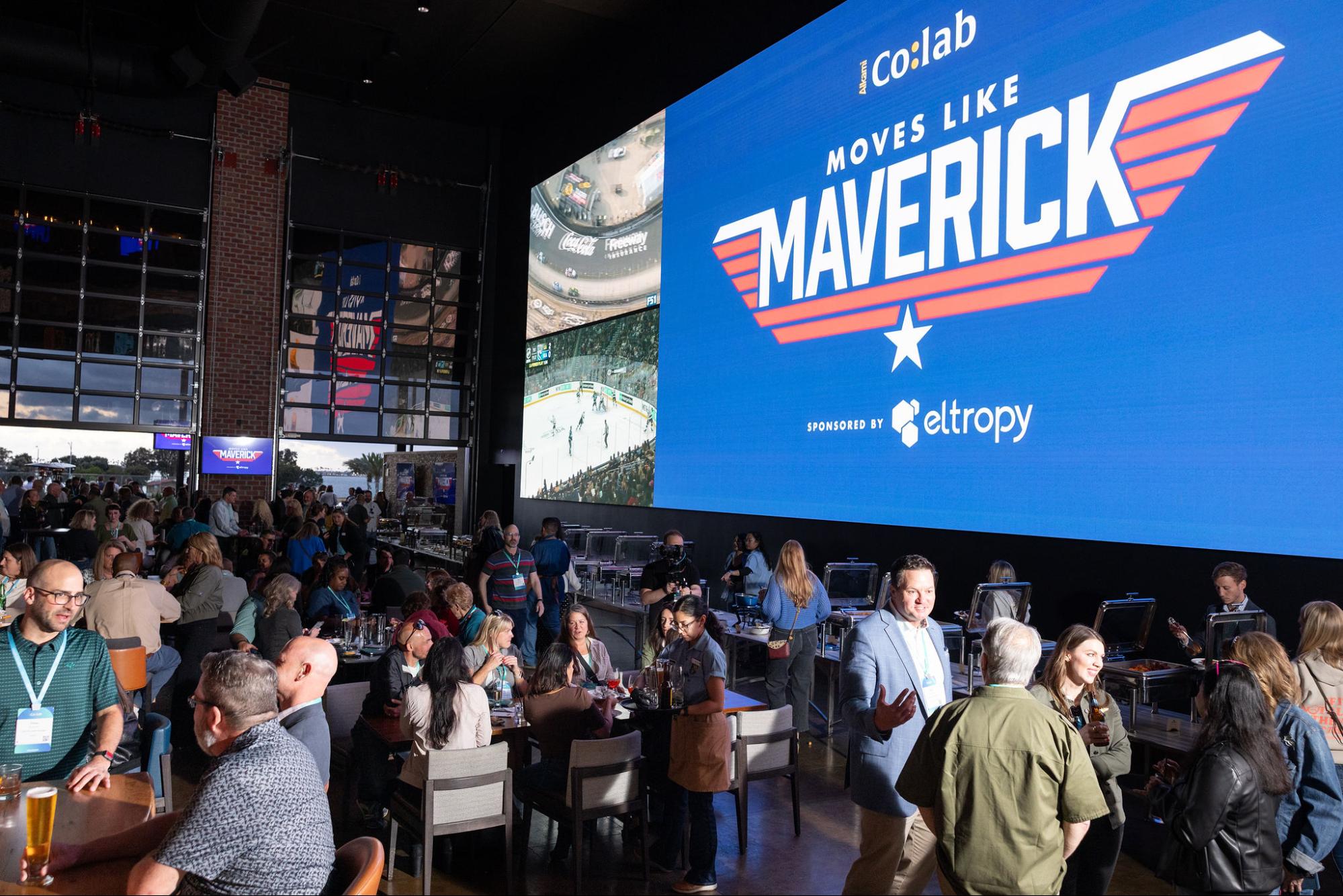 moves-like-maverick - Alkami Technology A packed restaurant with Alkami Co:lab attendees, a giant branded screen that reads Moves like Maverick sponsored by eltropy