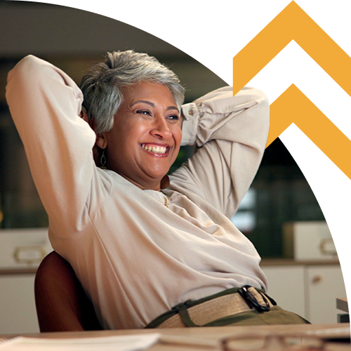 Smiling woman with short gray hair relaxing in an office chair with arms behind her head.