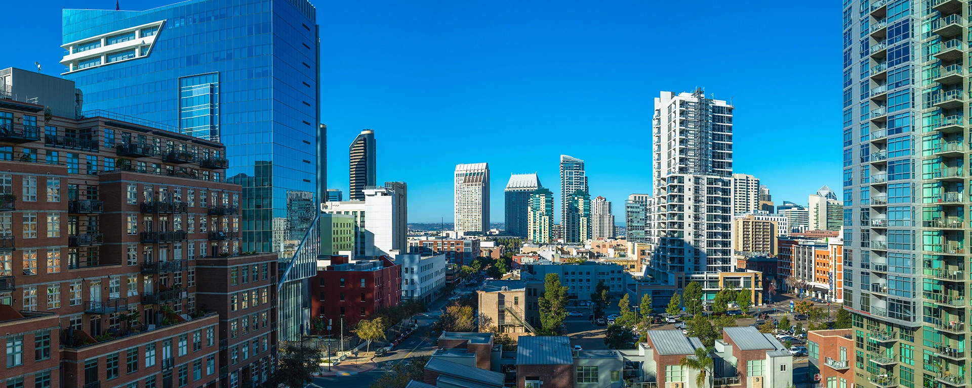 City skyline with modern glass high-rises under a clear blue sky, viewed from a rooftop perspective.