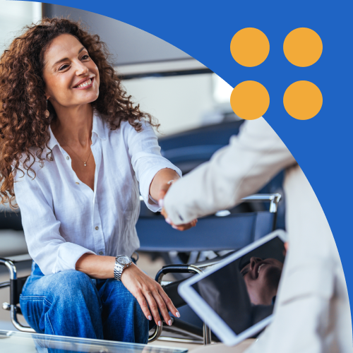 Smiling woman shakes hands with a salesperson in a car showroom, signaling a friendly greeting.