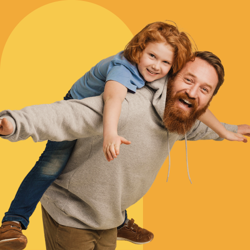 Bearded man giving a child a piggyback ride against an orange backdrop.
