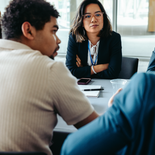 Professional woman wearing glasses sits at a conference table with colleagues, engaged in a meeting.