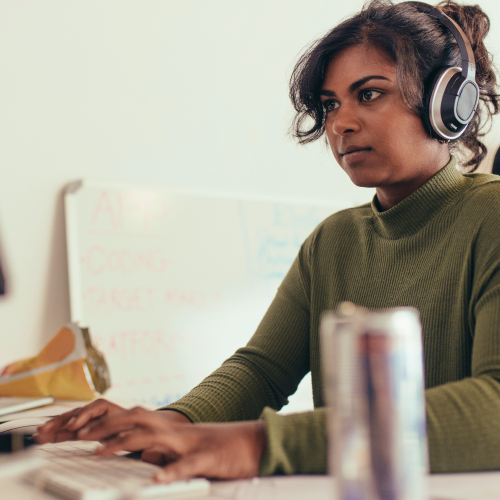 Woman wearing over-ear headphones, typing at a desk in a light-colored office.