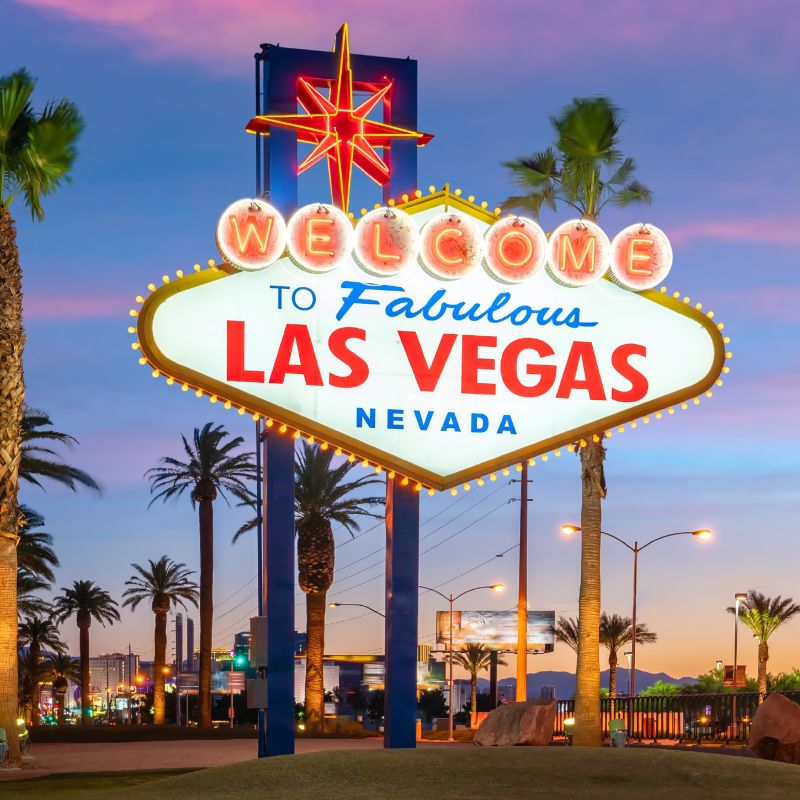 Welcome to Las Vegas sign lit up at dusk with palm trees nearby, iconic neon lights and 'Nevada' text